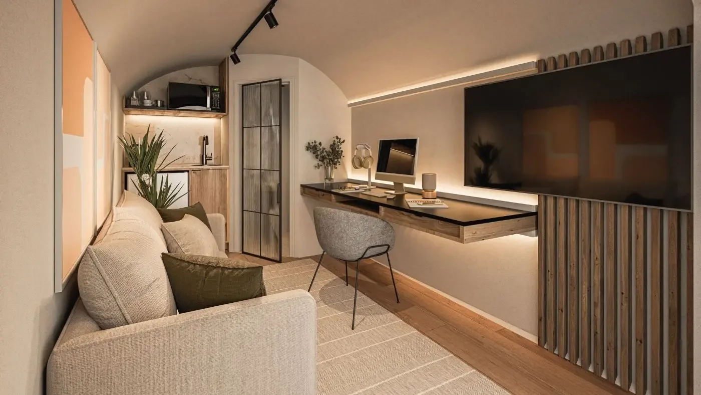 Garden office pod interior: desk and screen beneath the vaulted ceiling, kitchenette behind