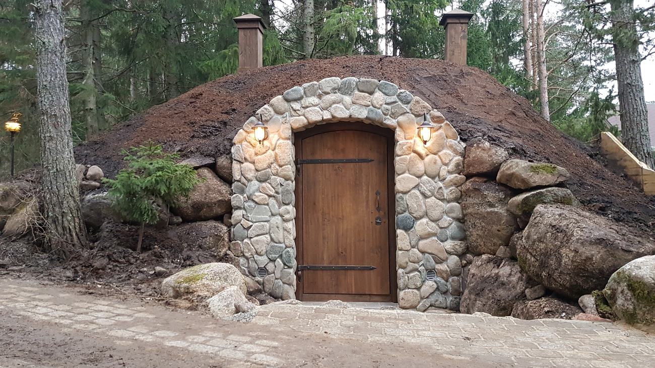 Stone hobbit house entrance with oak door set into an earth mound