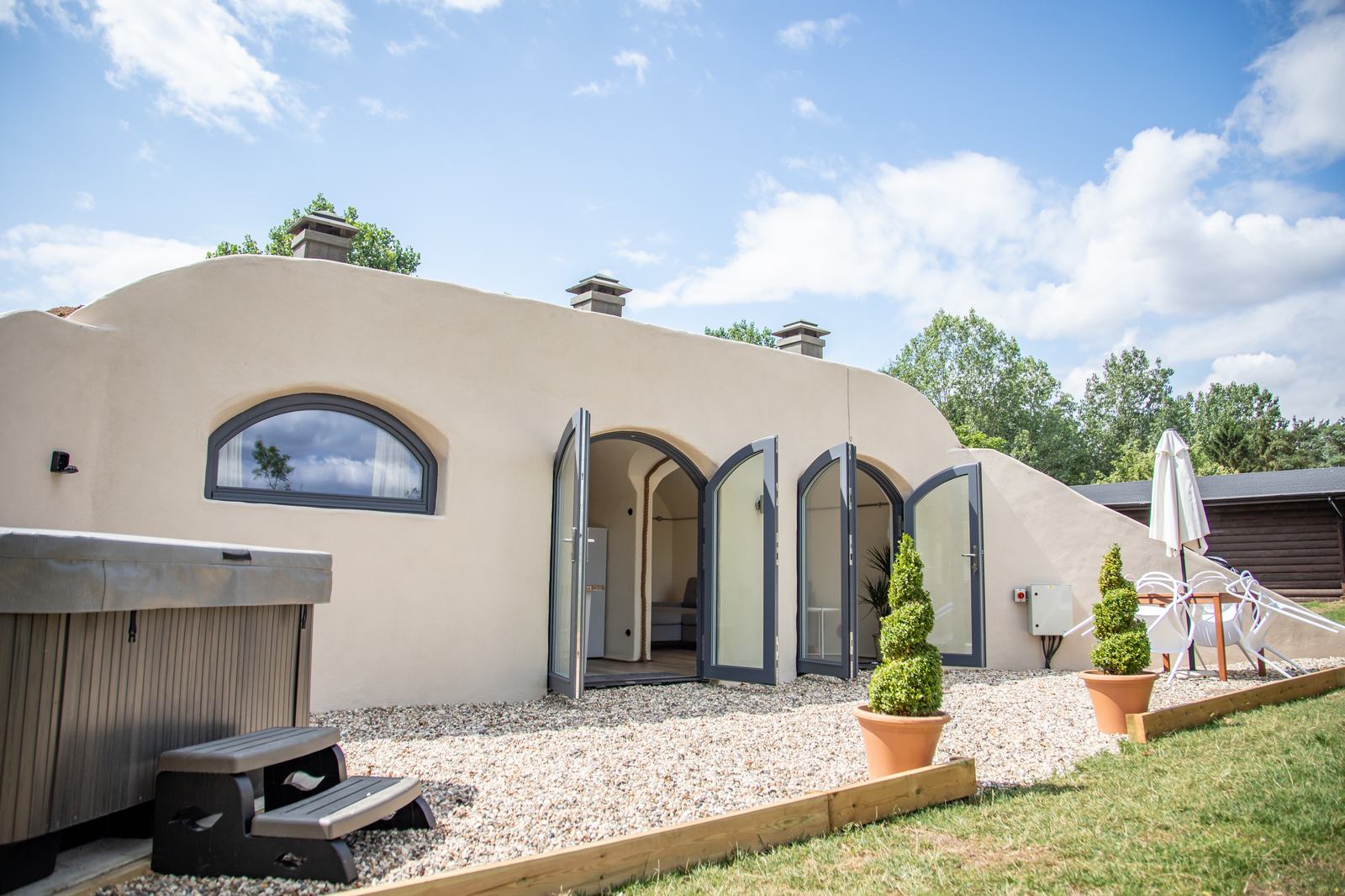 Earth-sheltered hobbit-style house in summer with arched glazed doors and hot tub